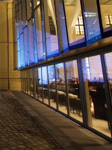 Glass courtyard in the evening (illuminated), view from the garden, persons at standing reception