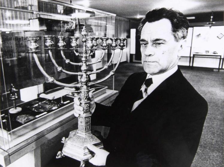 Black-and-white photo of a man in a suit holding a large Hanukkah menorah