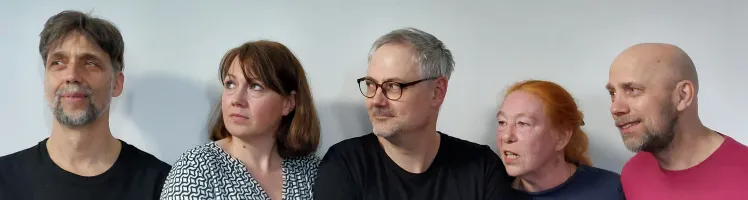 Fünf Menschen, davon 3 Männer und 2 Frauen, stehen nebeneinander. Sie blicken in die linke Richtung.