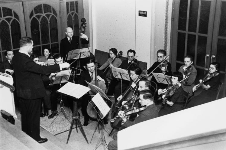 Schwarz-Weiß-Fotografie eins kleinen Orchesters mit Dirigenten