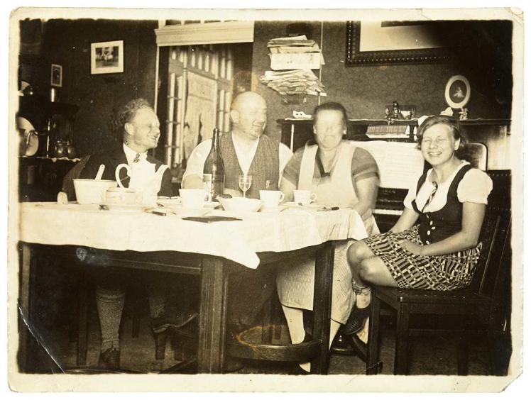 Schwarz-Weiß-Foto: vier lachende Personen an einem gedeckten Esstisch, die Gesichter großteils verschwommen