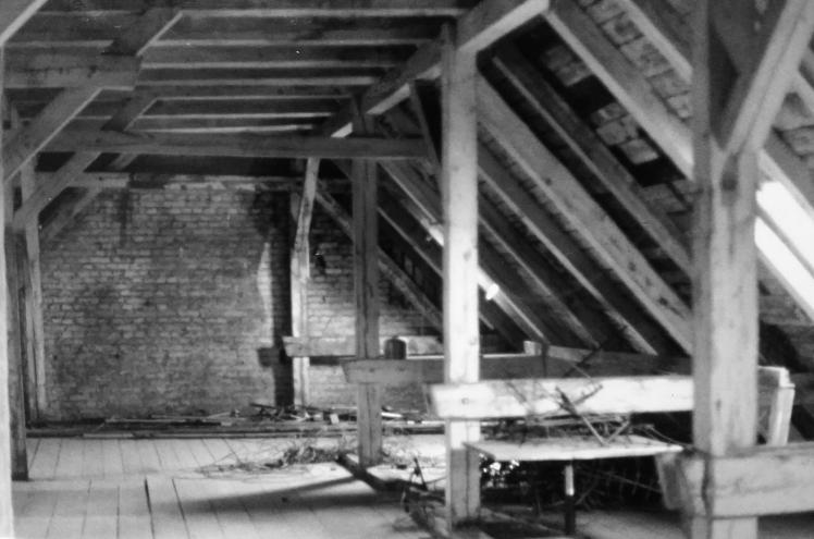 Schwarz-Weiß-Foto: Dachboden mit Holzbalken und Backsteinmauer