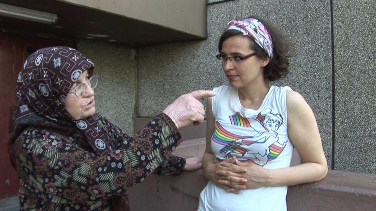 An older woman with glasses and headscarf (left in the picture) is talking to a younger woman who also wears glasses and is standing at the right edge of the picture.