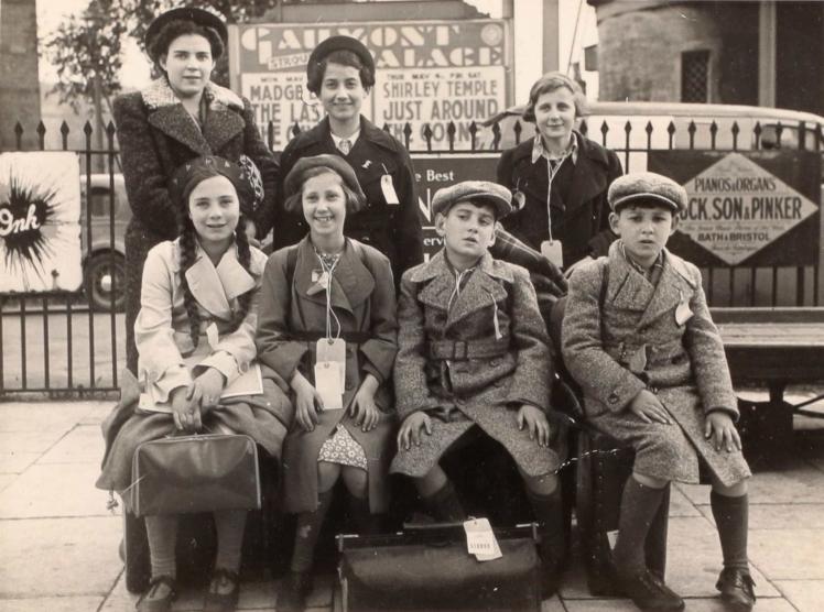 Schwarz-Weiß-Gruppenfoto von sieben Kindern mit Jacken und Gepäck