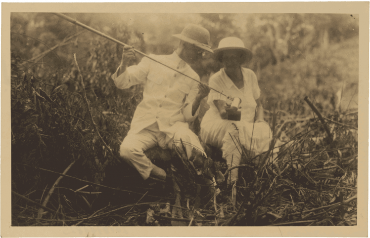 Historische Schwarz-Weiß-Fotografie  von zwei Forschern die im Gras sitzen.