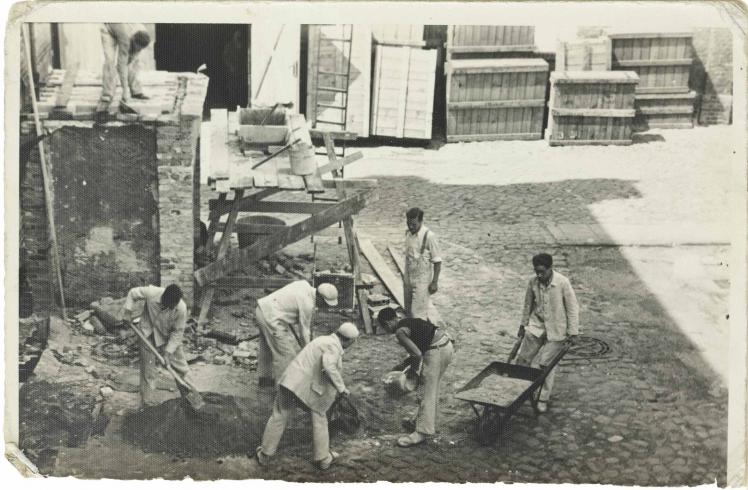 Seven men in working clothes and with wheelbarrow, shovels and other equipment (black and white photo)