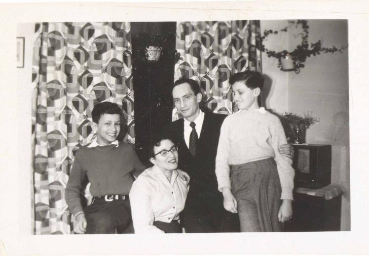 In the black-and-white photo, the family is in a room with patterned curtains and houseplants. All four are smiling or laughing. The image is very lively.