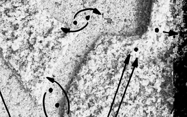 Black and white image of a section of sand with a Hebrew letter, superimposed by painted dots and arrows