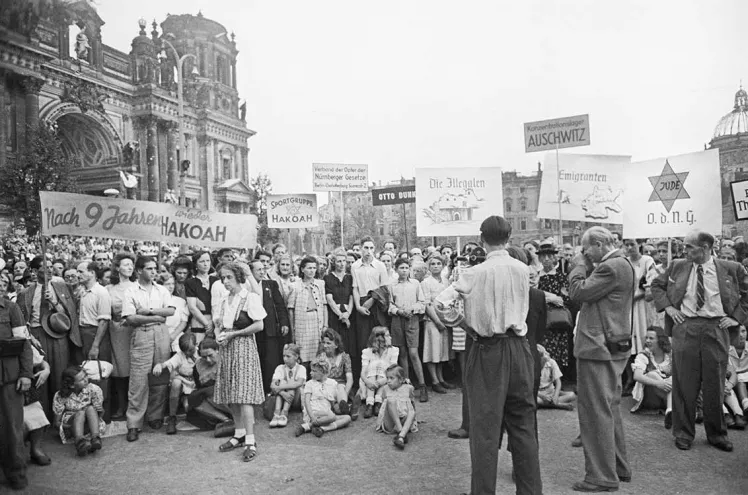 Schwarz Weiß Fotografie: Menschen auf einer Kundgebung vor dem zerstörten Berliner Dom halten Schilder in die Luft.