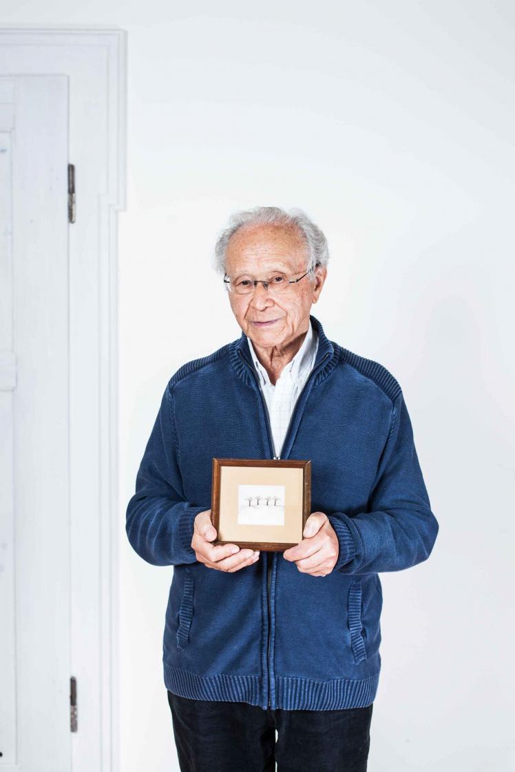 Elderly man holding a drawn picture with four trees in a frame in his hands