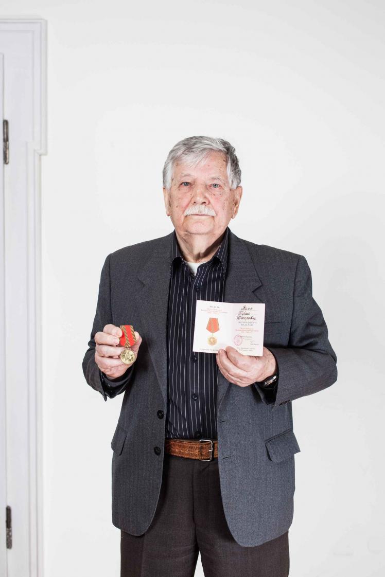Älterer Herr in dunklem Sakko hält Medaille und ein Dokument in Händen