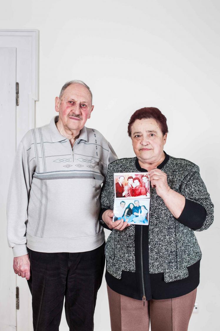 An elderly couple, the woman holding photos in her hands.