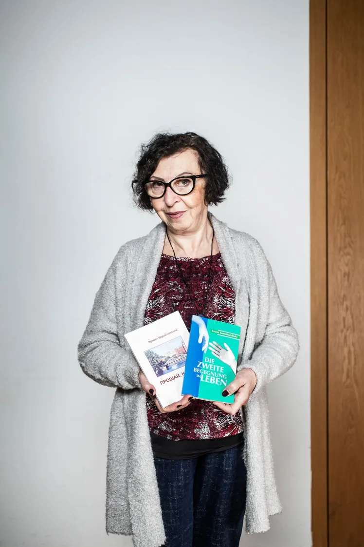 Eine Frau mit Brille hält zwei Bücher in der Hand und schaut freundlich in die Kamera.