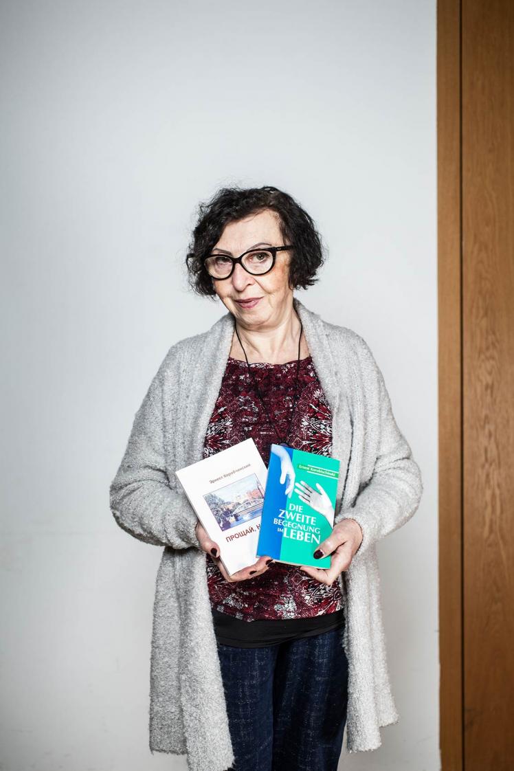 A woman with glasses holds two books in her hand and looks friendly into the camera.