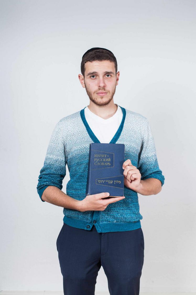 a young man holding a blue Russian-Hebrew dictionary. 