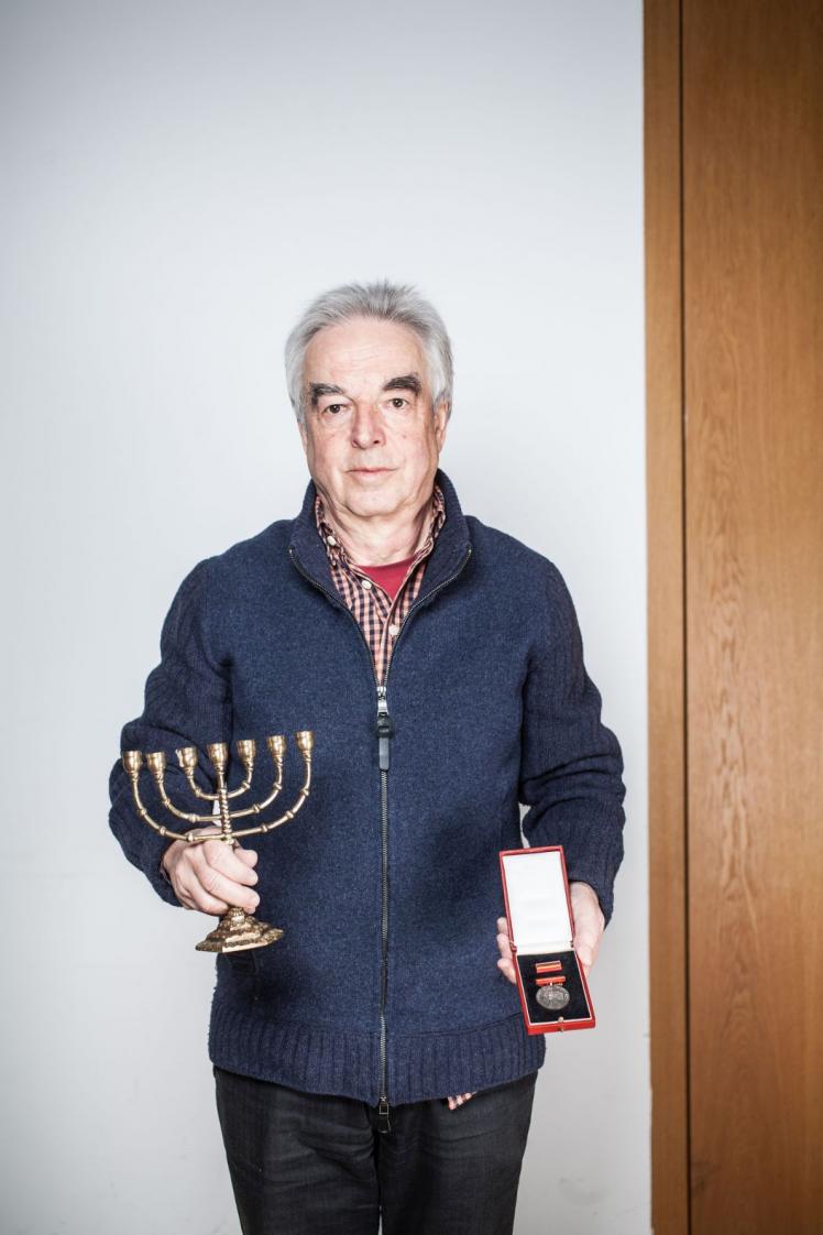 A gray-haired man holds a menorah in one hand and a medal in the other.