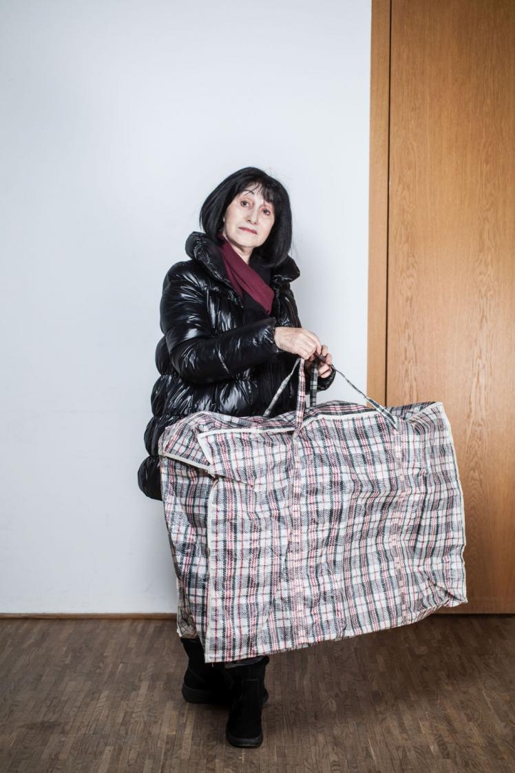 A woman in a thick winter jacket wears a huge plaid bag. 