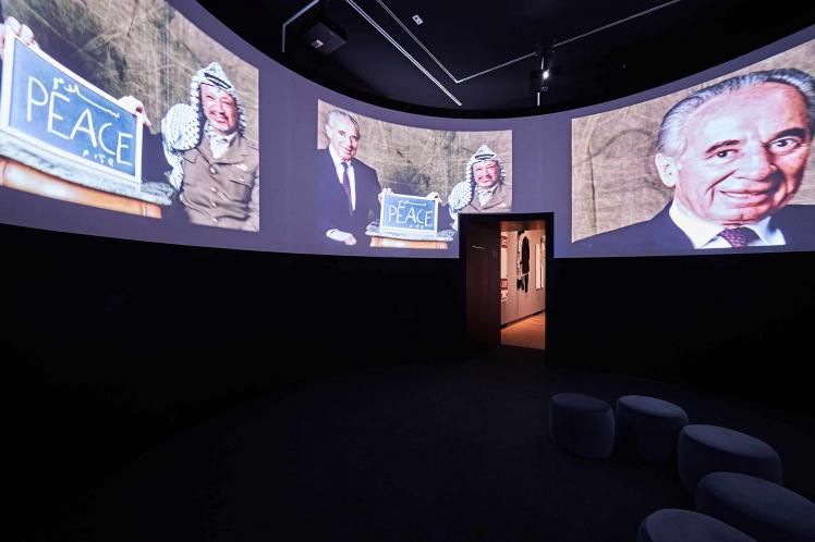 Room with a cinema screen showing Shimon Peres and Yasser Arafat with a sign that reads “peace.”