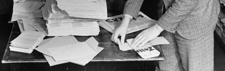 Schwarz-Weiß-Fotografie: Das Bild zeigt Hände, die Zeitungen für den Versand kuvertieren