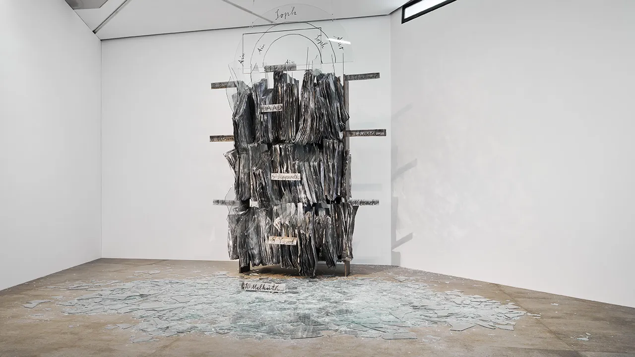In einem weißen Raum befindet sich eine Installation bestehend aus Papier und Scherben