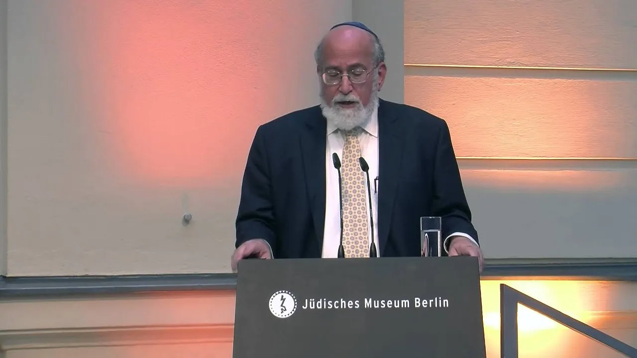 Ein Mann auf einer Bühne hinter einem Pult hält eine Rede.