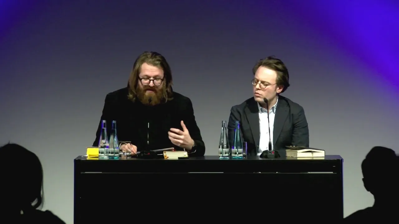 Zwei Männer sitzen an einem Podium und diskutieren miteinandner.