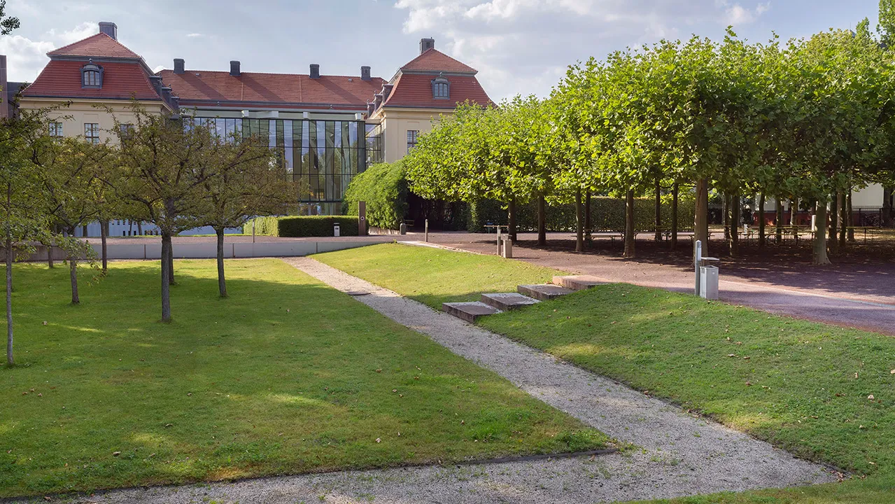 Außenansicht des Altbaus und Glashofes, im Vordergrund sieht man einen schönen, ordentlichen Garten